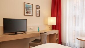 A hotel room with a bed, a desk with a television, a chair, a lamp, and two framed pictures on the wall. - Sunday Hotel Stade Widukind Single Room (Stade)