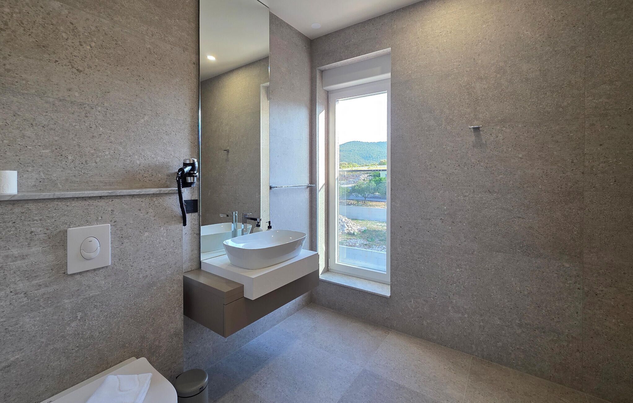 A modern bathroom with a large mirror, a built-in sink, and a window offering a view of the outdoors.