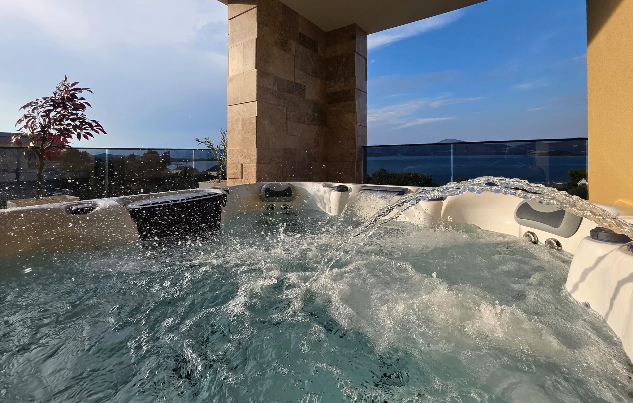 A hot tub with water jets, a stone pillar, and a view of the sky and water.
