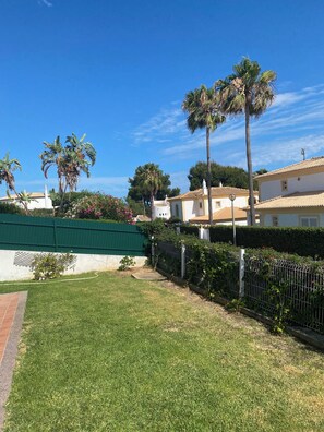 A residential area with a well-maintained lawn, palm trees, and a green fence. - Villa Med - private pool, garden, barbecue, air conditioning, and ocean view (Olhos de Água)