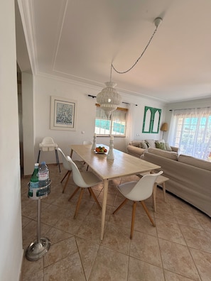 Een eethoek met een tafel, stoelen, een kroonluchter en een raam met gordijnen.