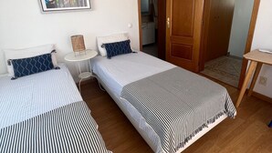 Ein Zimmer mit zwei Betten, einem kleinen Tisch, einer Wand-Klimaanlage und einer Tür zu einem anderen Raum.