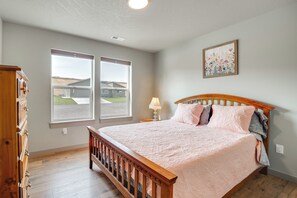 A bedroom with a wooden bed, two windows, a nightstand, a lamp, and a painting on the wall.