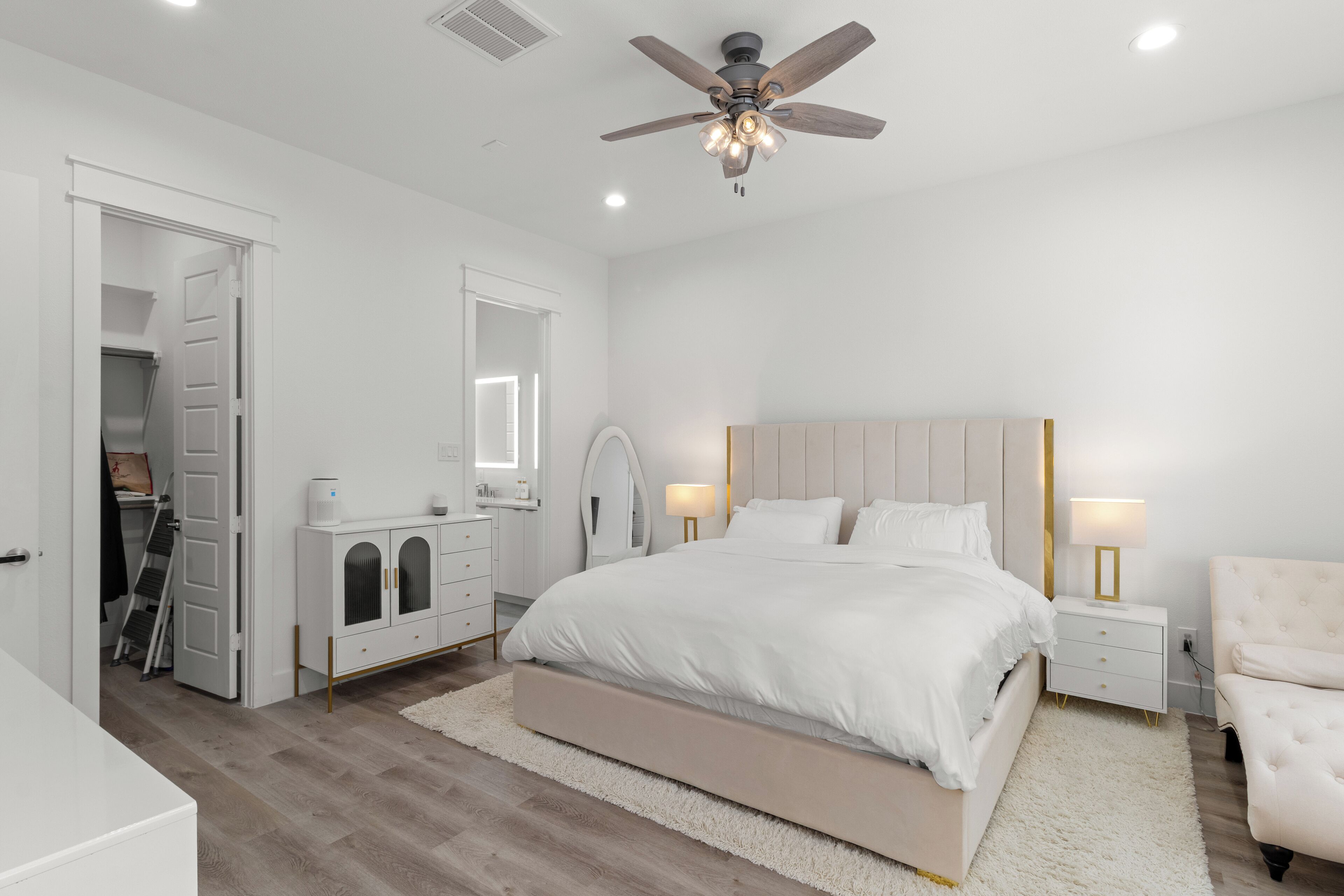 A modern bedroom with a large bed, bedside tables, a ceiling fan, and a walk-in closet.