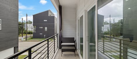 A balcony with a metal railing, a bench, and a view of neighboring buildings.