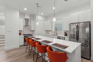 Eine moderne Küche mit weißen Schränken, einem Edelstahlkühlschrank und orangefarbenen Barhocker.