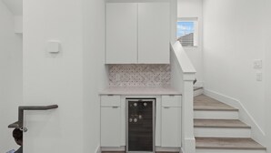 A narrow hallway with a white door, a small kitchen area with a microwave, and a staircase with wooden steps. - Luxurious 3-Bedroom Home In Downtown Houston Area (Houston)