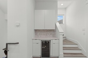 Ein schmaler Flur mit einer weißen Tür, eine kleine Küchenzeile mit einer Mikrowelle und eine Treppe mit Holzbodenstufen.