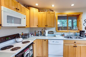 A kitchen with wooden cabinets, a microwave, a stove, a dishwasher, and a window with a view of trees.