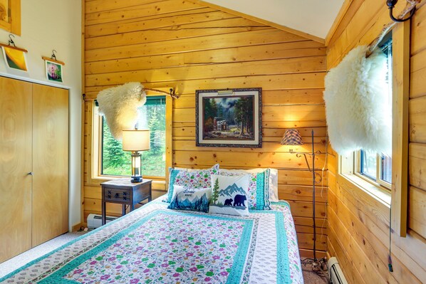 A wooden cabin bedroom with a bed, a painting, and a window with a view of trees.