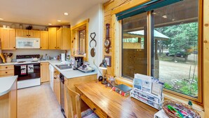 Une cuisine avec des meubles en bois, un four à micro-ondes et une grande fenêtre donnant sur une forêt.