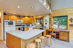 Cocina moderna con armarios de madera, una isla central, taburetes de bar y vistas al exterior a través de un amplio ventanal.