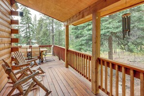 A wooden deck with outdoor seating and a view of a forest.