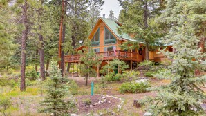 Une cabane en rondins dotée d’une terrasse, entourée d’une forêt dense.
