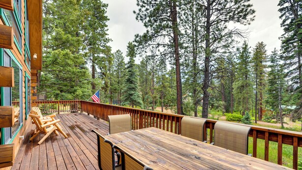 Une terrasse en bois avec une table et des chaises, entourée de grands pins.