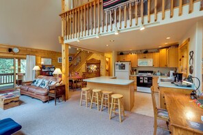 Un amplio salón con una escalera de madera, una cocina con electrodomésticos modernos y una zona de estar acogedora con chimenea.