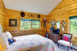 Quarto de cabana com cama, penteadeira, televisão e diversos enfeites.