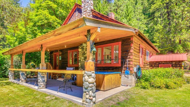 Eine Holzblockhütte mit Veranda, Steinpfeilern und einem Whirlpool.