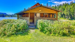 Eine Holzhütte mit Veranda, umgeben von üppiger Vegetation und einem See.