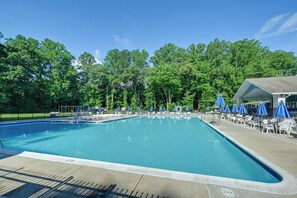 Une piscine rectangulaire avec une terrasse carrelée, entourée de chaises longues blanches et de parasols bleus.