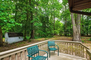 Une terrasse en bois avec deux chaises, entourée d’un feuillage verdoyant et touffu, et un petit abri de jardin à proximité.