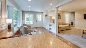 A spacious living room with a large wooden table, wicker chairs, a beige sofa, and a television.