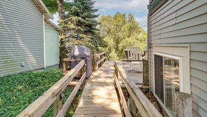 A wooden deck leading to a covered outdoor seating area with a view of a house and trees.
