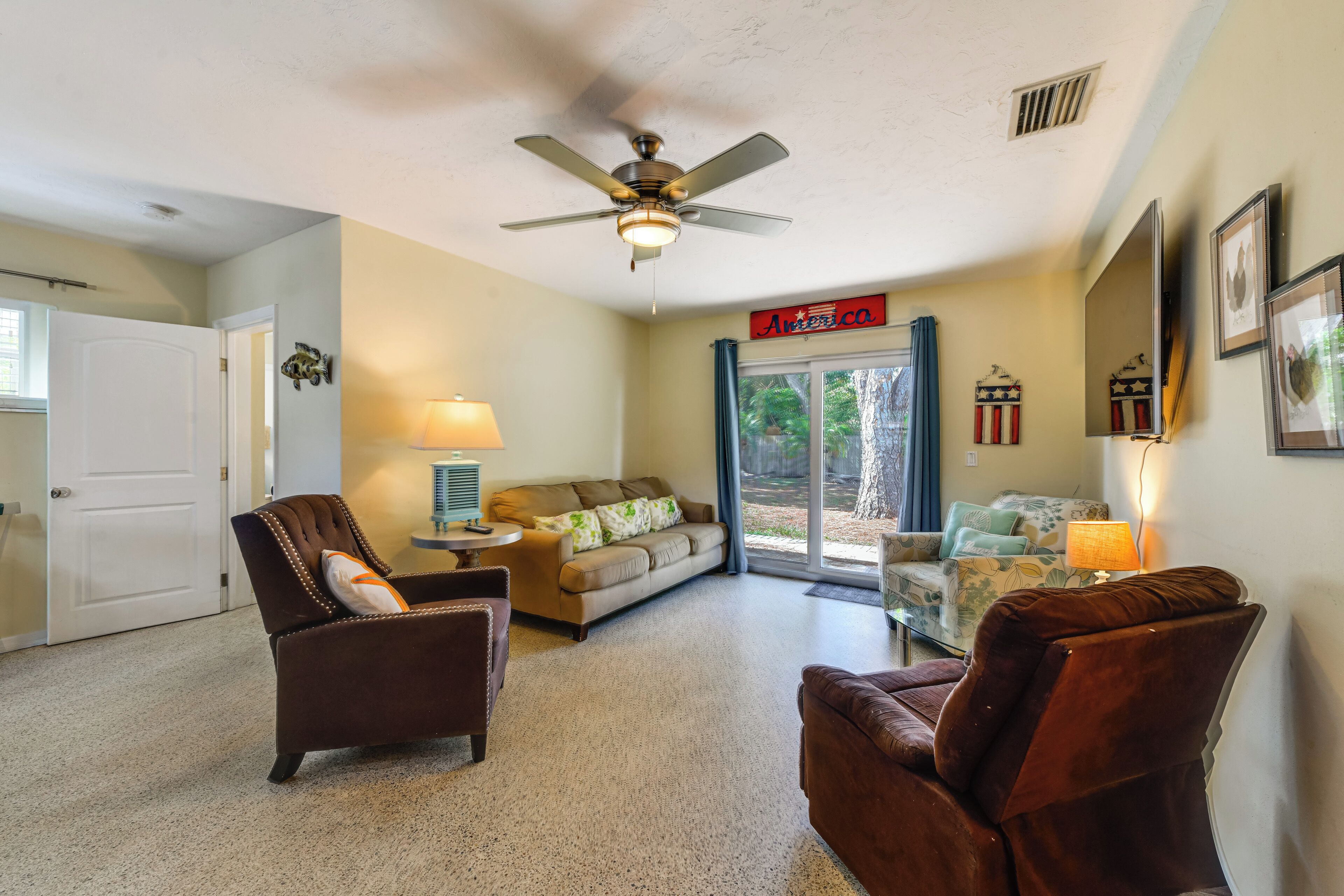A living room with a ceiling fan, a sofa, two armchairs, a coffee table, and a window with a view of the outdoors.
