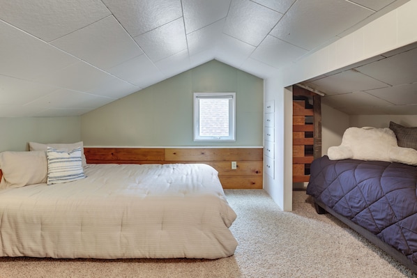 A bedroom with a sloped ceiling, a window, a wooden headboard, a bed with a white comforter, a purple comforter bed, and a small wooden dresser. - Walk to Beaches! Lincoln City Family Home w/ Yard (Lincoln City)