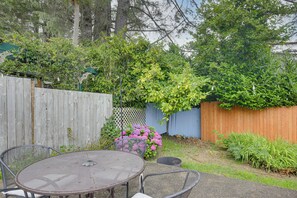 A patio with a round metal table and chairs, surrounded by a wooden fence and lush greenery. - Walk to Beaches! Lincoln City Family Home w/ Yard (Lincoln City)