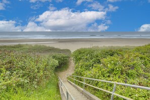Ein Küstenpfad, der zu einem Strand führt, mit blauem Himmel und Meer.