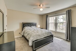 Ein Schlafzimmer mit Bett, Deckenventilator, einem Fenster mit Vorhängen und einem Schminktisch.