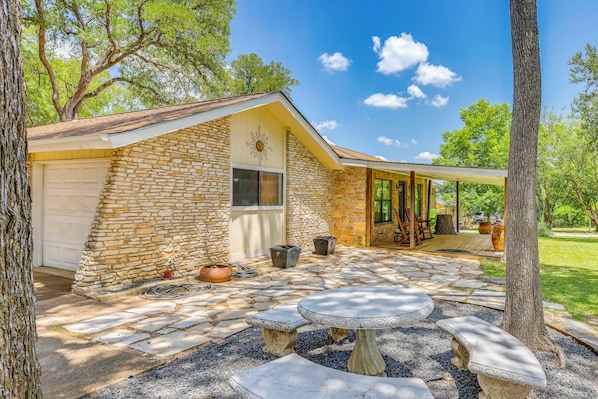 Una casa de piedra con garaje, un porche cubierto y un patio de piedra con una mesa circular.