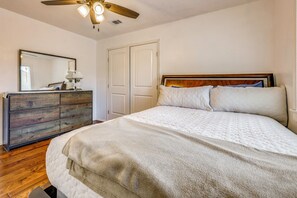 A bedroom with a wooden dresser, a bed with a quilted cover, a ceiling fan, and a white door. - Luxe Hill Country Home w/ Resort-Style Pool! (Buda)