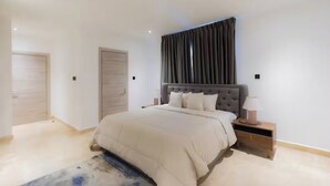 A bedroom with a large bed, a nightstand, a lamp, and a window with curtains. - Wentworth (Accra)