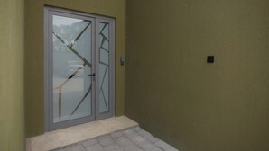 A door with a glass panel and a metal handle, set in a building with a textured wall. - Wentworth (Accra)