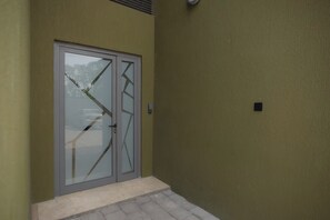 A door with a glass panel and a metal handle, set in a building with a textured wall. - Wentworth (Accra)