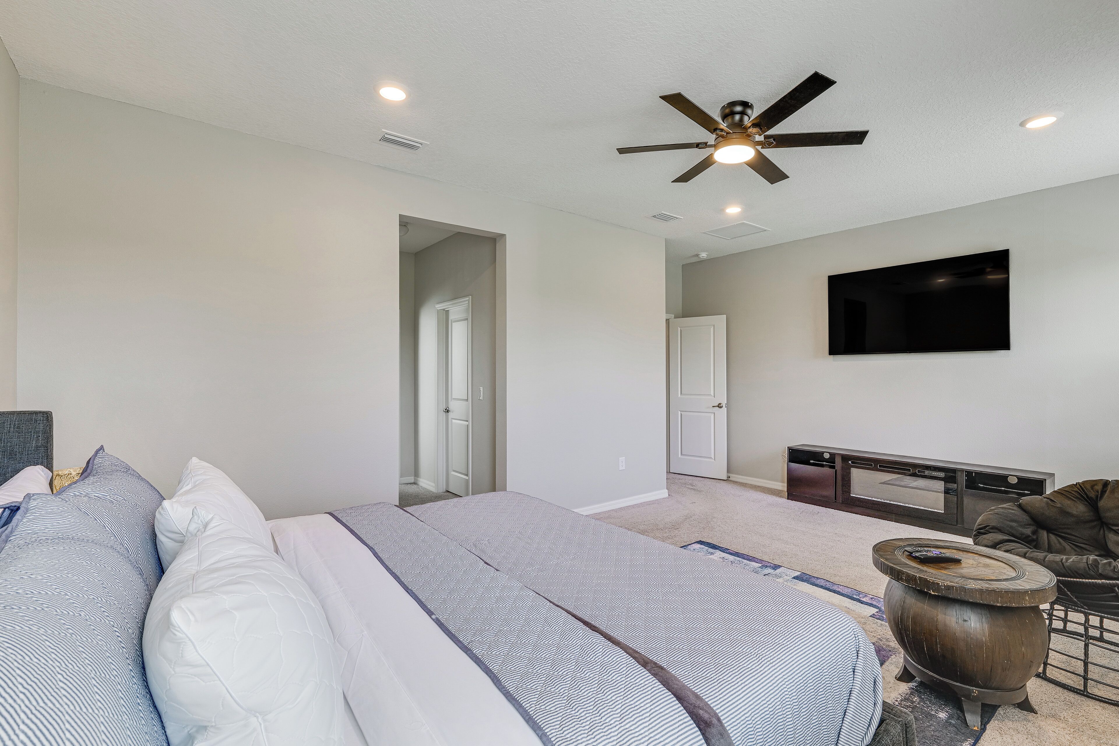 A bedroom with a bed, a ceiling fan, a flat-screen TV, and a fireplace.