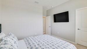 Una camera da letto con un letto, una televisione a parete e una porta che dà su un'altra stanza.