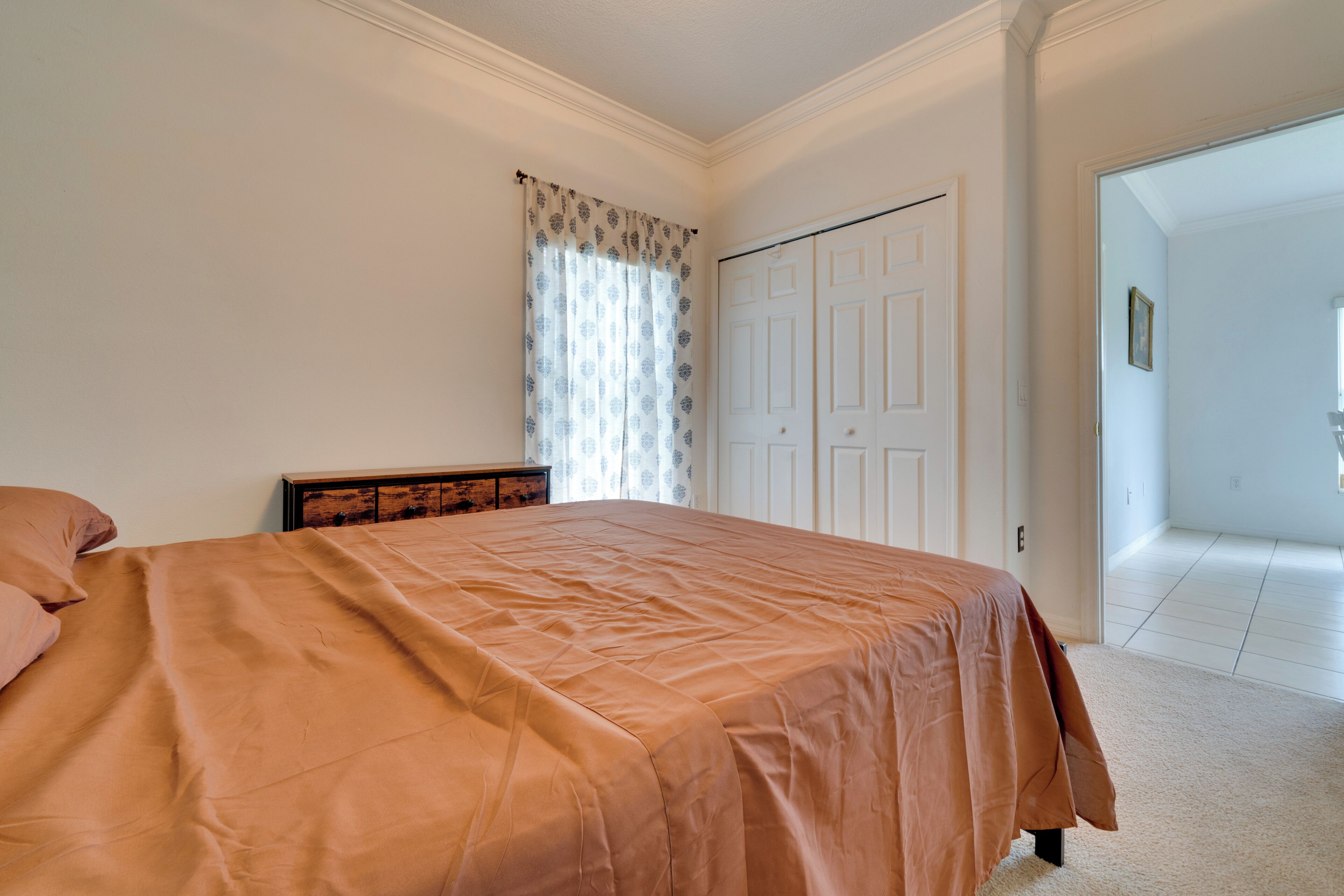 A bedroom with a bed, a dresser, a door, and a window with curtains.