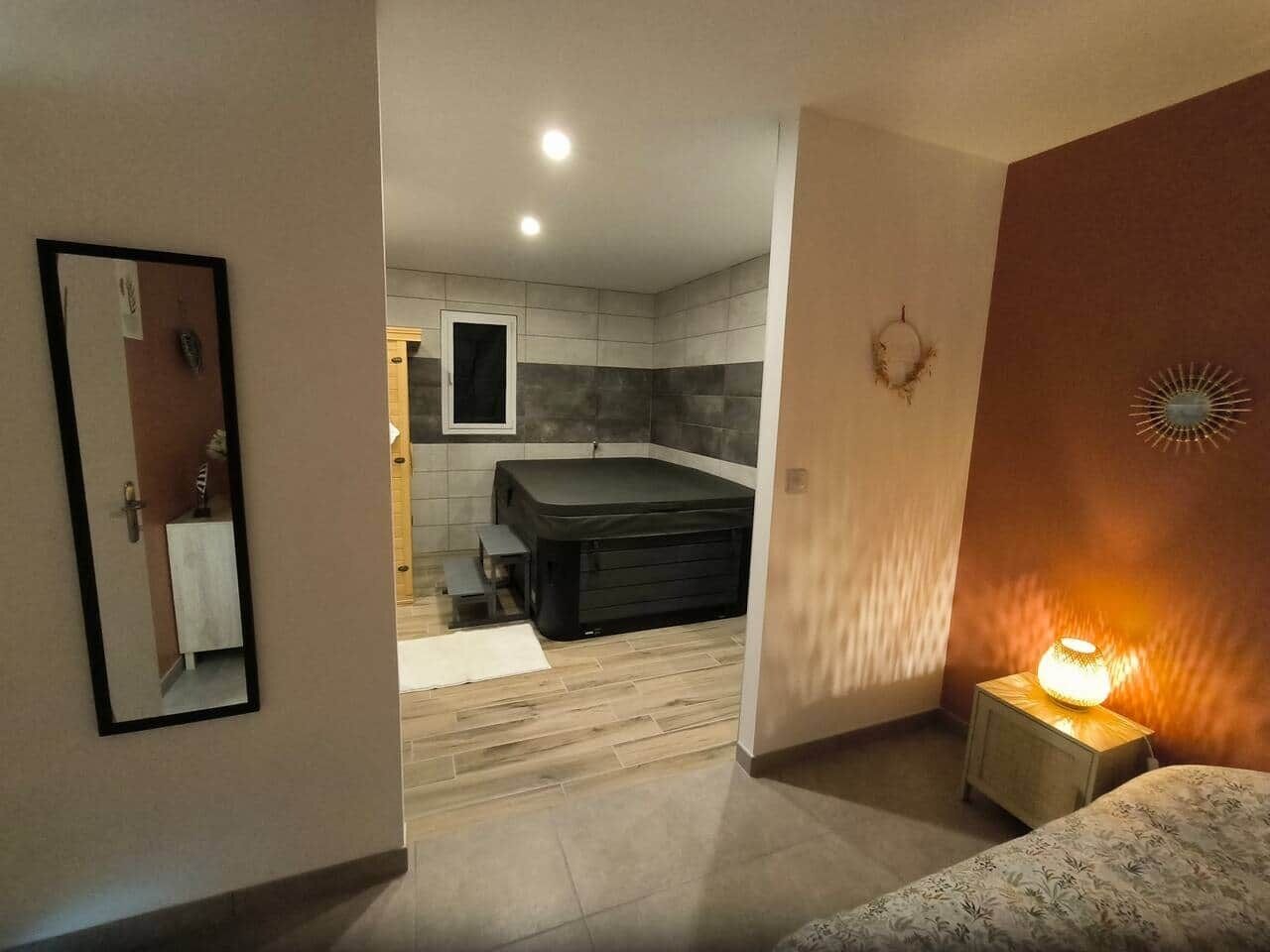 A modern hotel room with a bed, a small bedside table with a lamp, a large window, and a view of the bathroom.