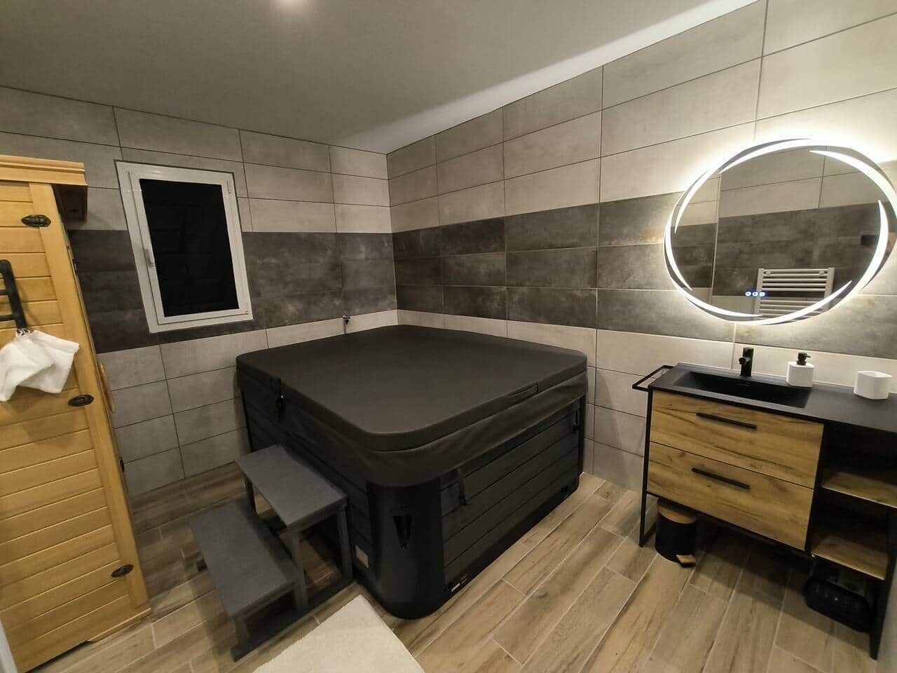 Una habitación compacta con hidromasaje integrado, un ventanal pequeño, un tocador con espejo y una puerta de madera.