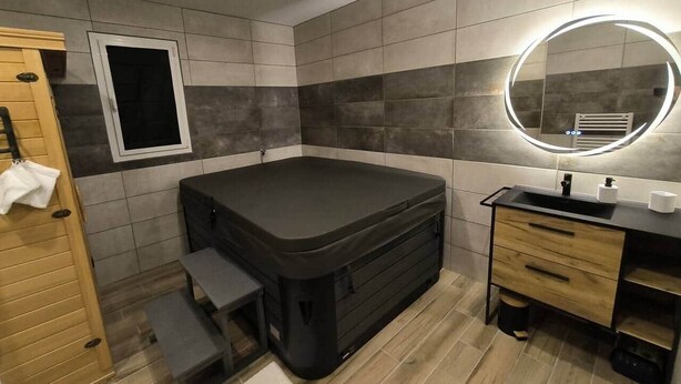 A compact room with a built-in hot tub, a small window, a vanity with a mirror, and a wooden door. - Vacation rental with private spa, jacuzzi, and sauna in the Baie de Somme. "Bubbles of Happiness" (Cahon)