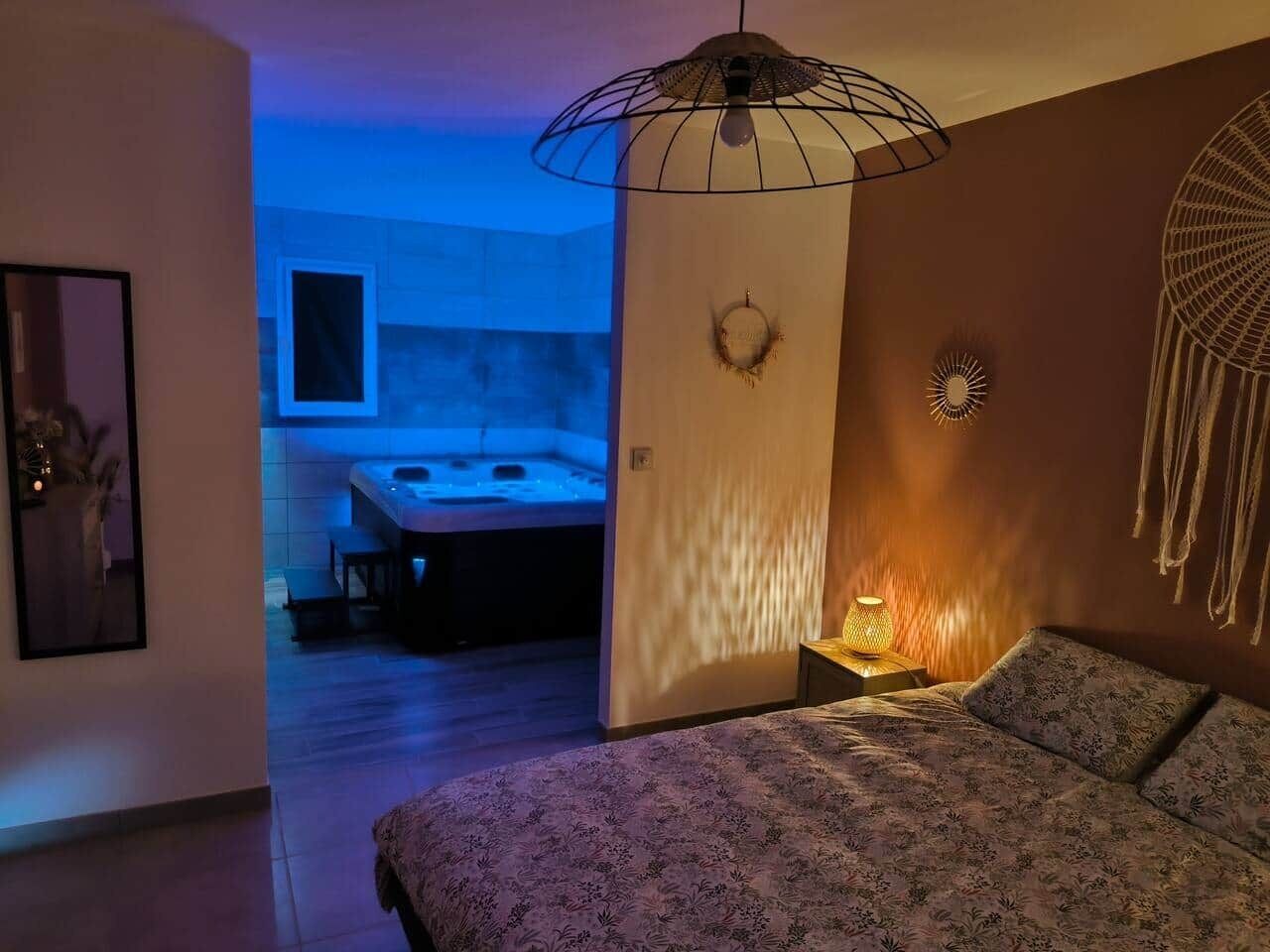 Un dormitorio con cama, una lámpara de noche, una luz en la pared y vista al baño.