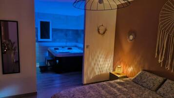 Un dormitorio con cama, una lámpara de noche, una luz en la pared y vista al baño.