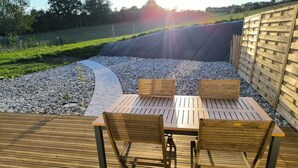 An outdoor wooden deck with a table and chairs, surrounded by a gravel path and a wooden fence.