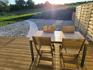Una terraza de madera al aire libre con una mesa y sillas, rodeada por un camino de grava y una valla de madera.