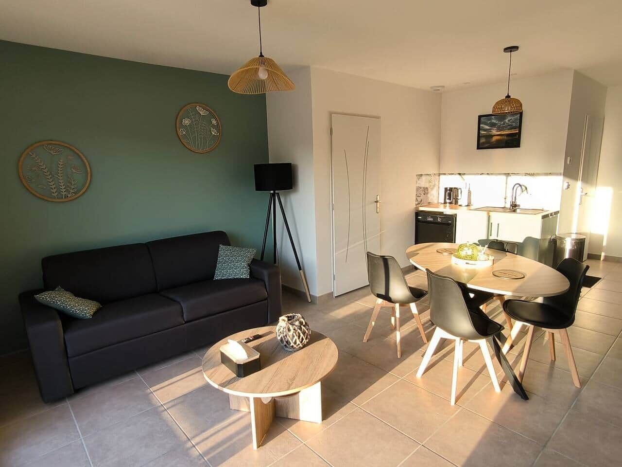 Una sala de estar moderna con sofá, mesa de centro y comedor con sillas. Se ve una cocina al fondo con fregadero y estufa.