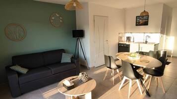 Una sala de estar moderna con sofá, mesa de centro y comedor con sillas. Se ve una cocina al fondo con fregadero y estufa.