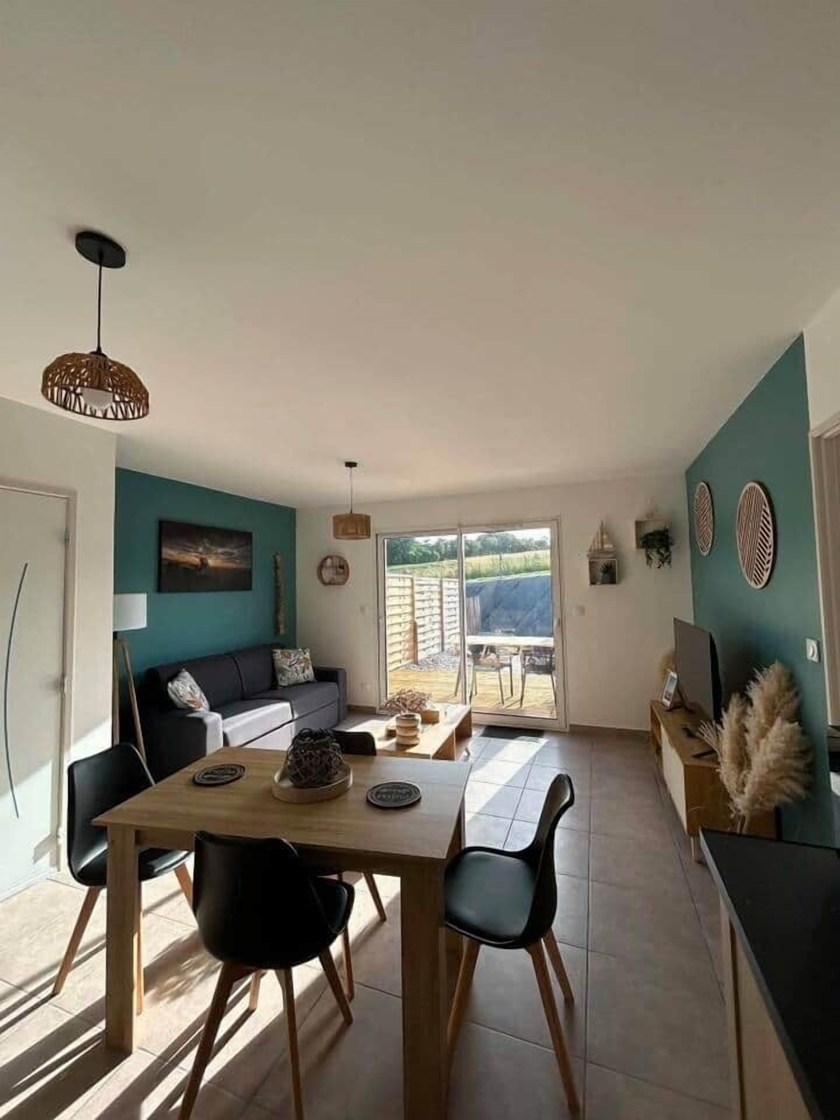A dining area with a wooden table and chairs, a sofa, and a view of the outdoors through a sliding door.